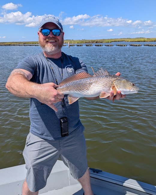 Jeff Plumlee holding a red drum on a boat in Louisiana coastal marsh.