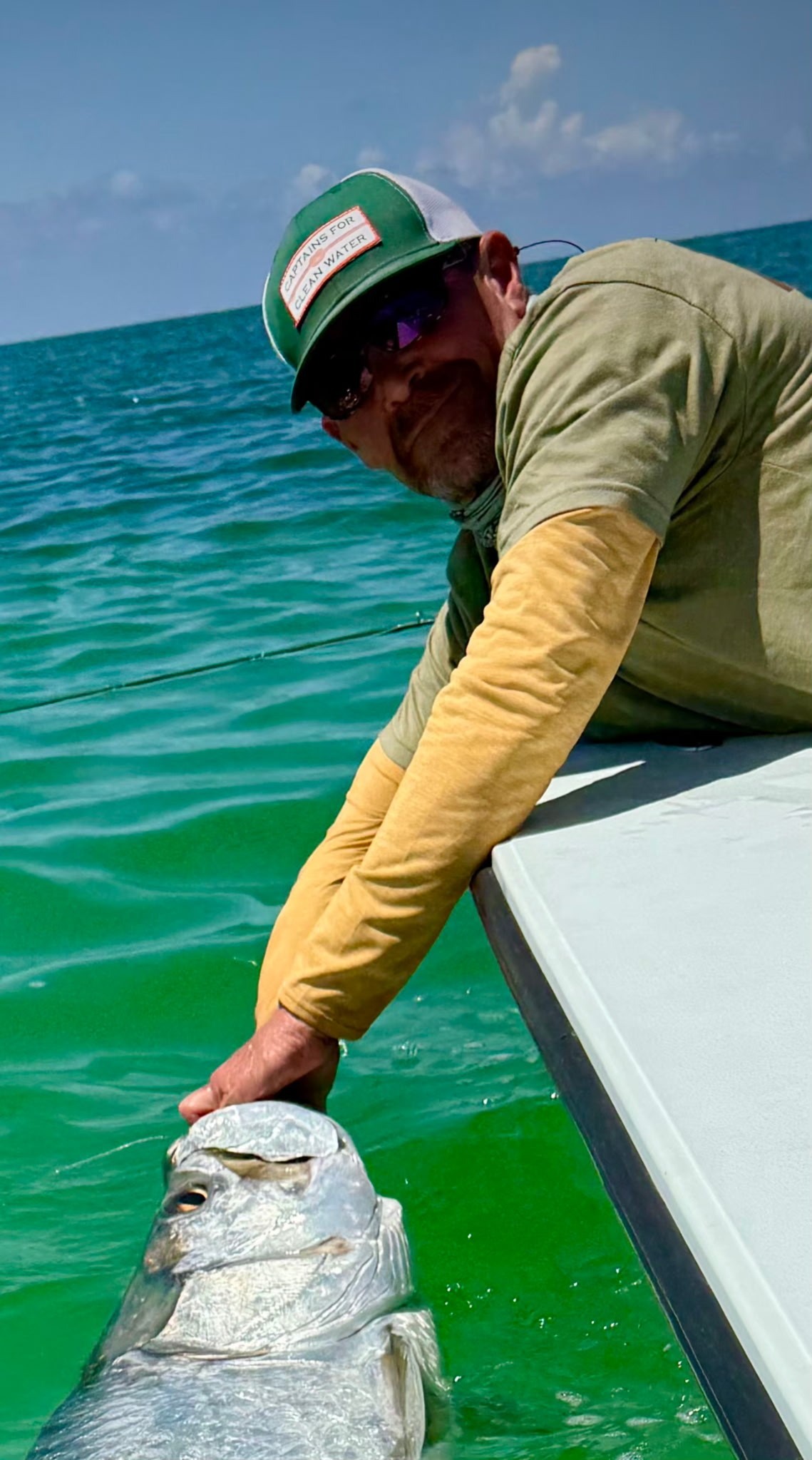 Rick Owens leaning over the side of a boat while releasing a tarpon.